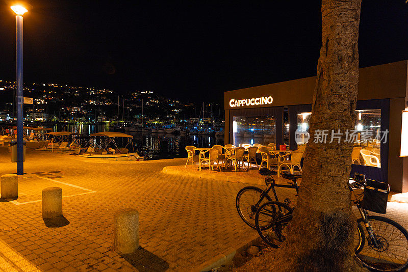 安德拉克斯港(Puerto Andratx)的船坞，背景是群山中灯火通明的房屋，前景是夜晚空荡荡的餐厅